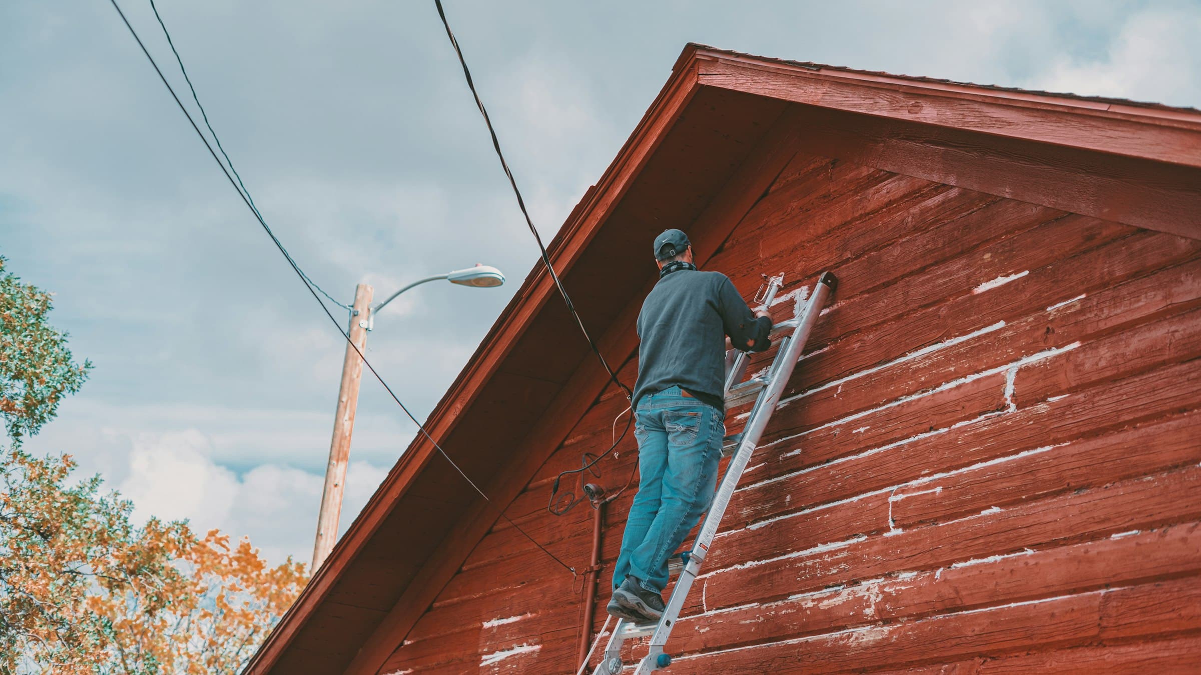Crew member on a ladder working the gable end of a rust-red wooden house