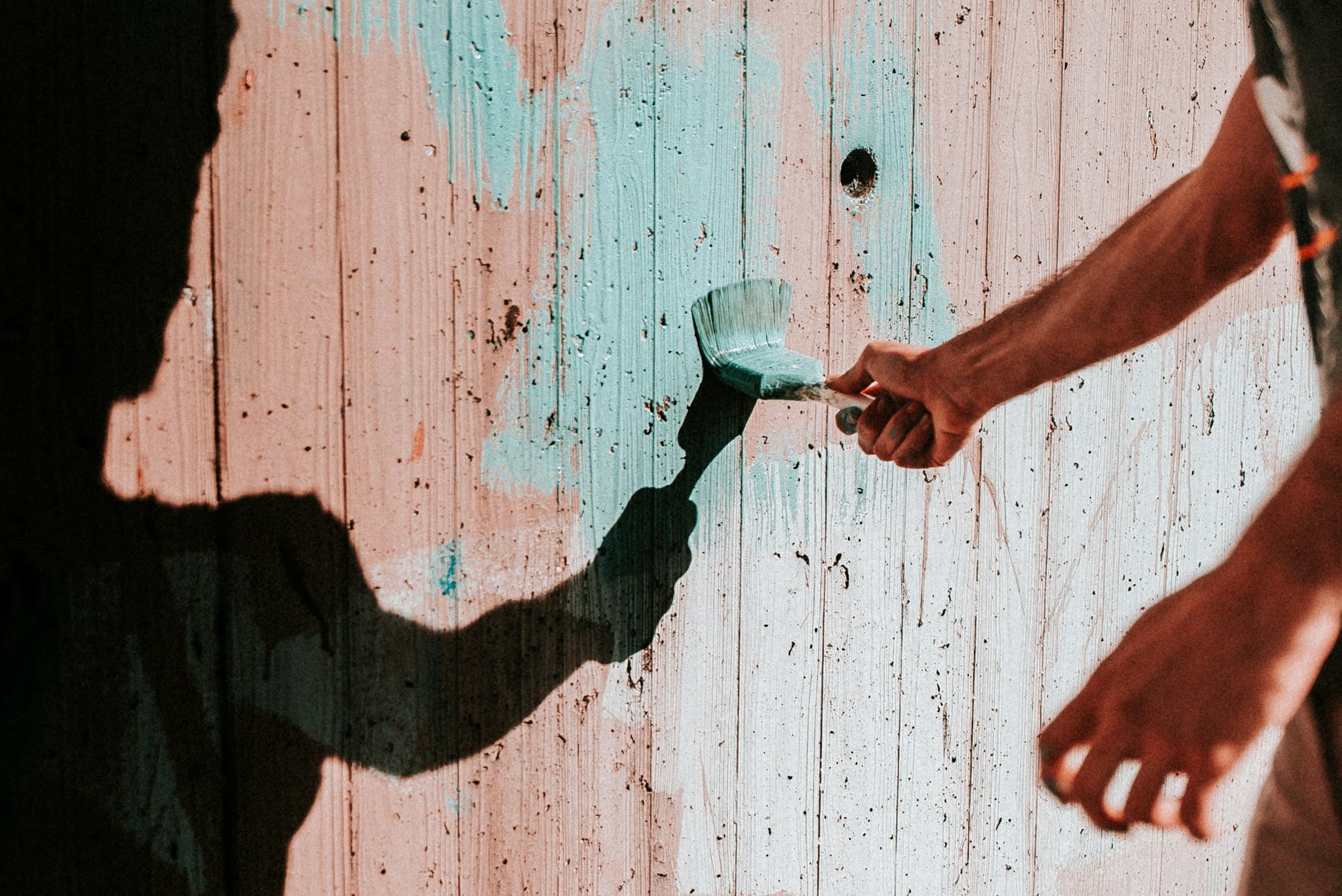 A hand brushing fresh paint onto weathered plank boards in low sun