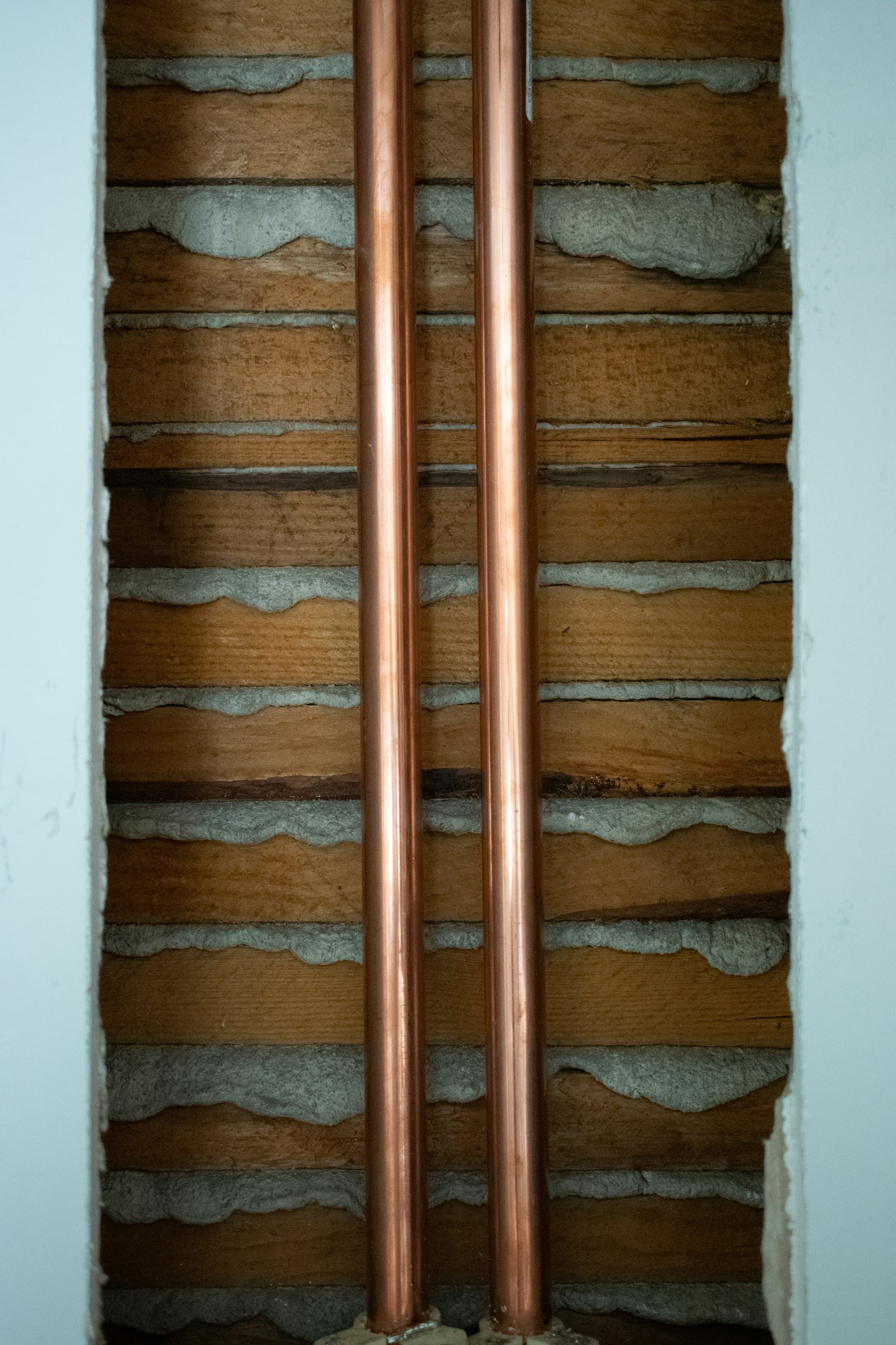 Two new copper water lines set into an opened wall of old wood lath